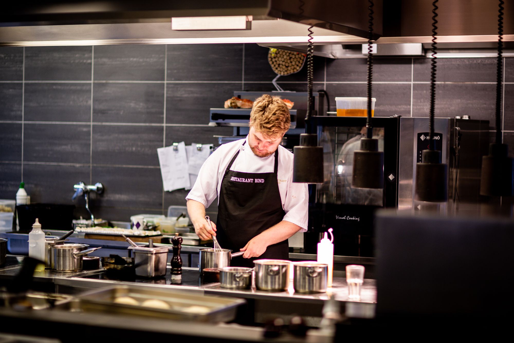 Chef working a stainless commercial kitchen line under an industrial hood