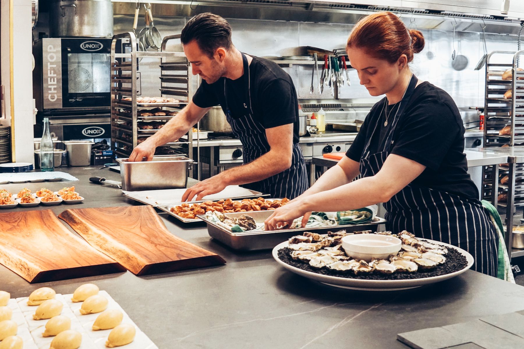 Chefs working a commercial kitchen line with stainless equipment and professional ovens