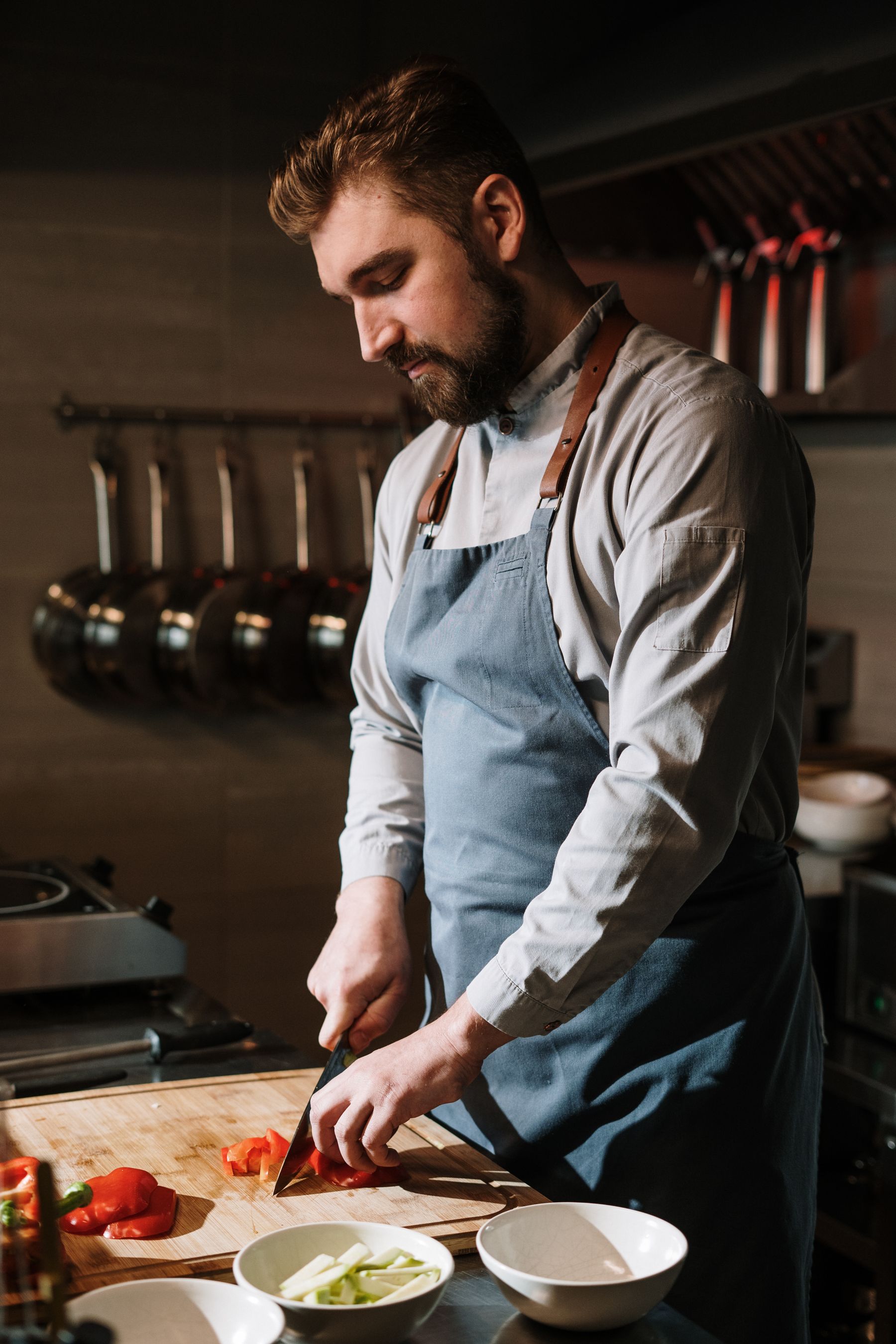 Chef working at a stainless range with hanging sauté pans in a commercial kitchen